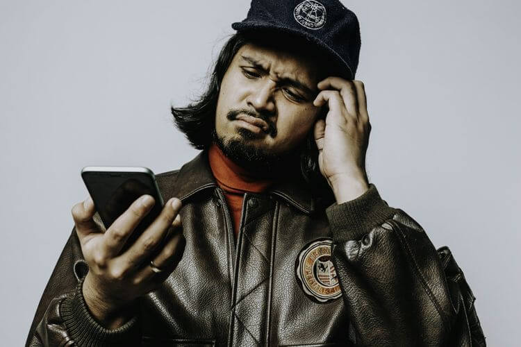 Petra Sihombing mengenakan topi dan jaket kulit menatap layar smartphone